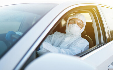 Man in Hazmat suit, protective gloves and goggles driving car during an epidemic in quarantine city. Covid- 19. Prevention of spreading global pandemic pneumonia virus.