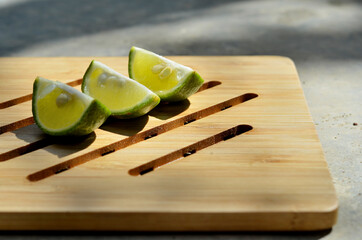 three slices of limes (Citrus × aurantiifolia) on a wooden tray. commonly used in tropical...