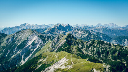 A panoramic view on the Alps from the top of mountain in Slovenia. Clear and sunny day. Sharp peaks around. A bit of haze in the valley. Outdoor activity. Lush green slopes with barren peaks. Calm