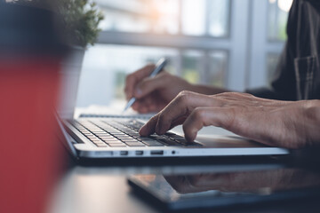 Close up of man hand typing and surfing the internet on laptop computer and writing on notepad at home office, 