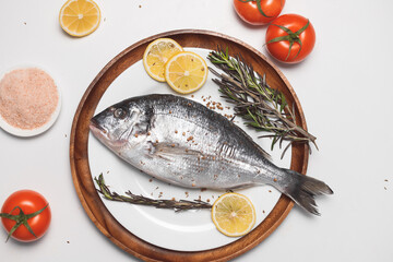 Raw dorada fish or gilt-head bream served on white plate on white background, flat lay, top view