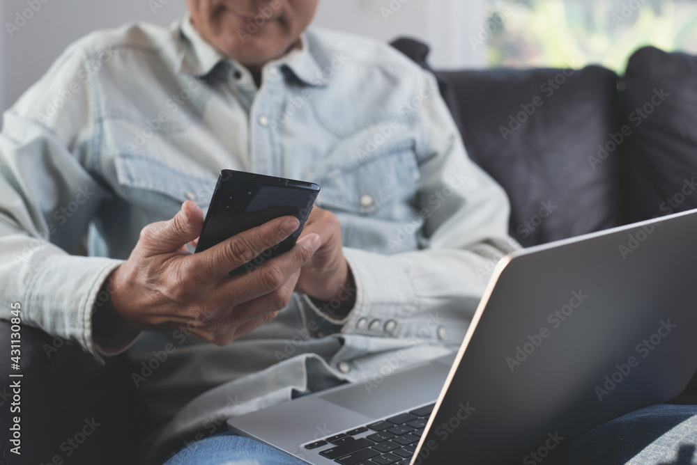 Poster man wearing casual clothes sitting on sofa using mobile phone browsing the internet and laptop compu