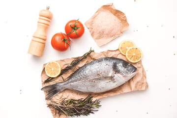 Raw dorada fish or gilt-head bream on ice with lemon, tomato, rosemary and salt over white background, flat lay, top view