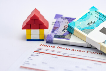 Close up of a blocks house near money bundles on home insurance form.