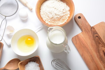 Fototapeta na wymiar Frame of food ingredients for baking on a white background. Flour, eggs, sugar and milk in white and wooden bowls . Cooking and baking concept.