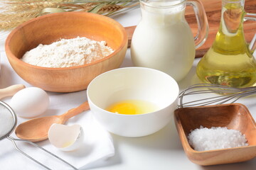 Frame of food ingredients for baking on a white background. Flour, eggs, sugar and milk in white and wooden bowls . Cooking and baking concept.