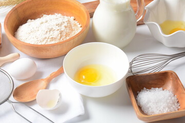 Frame of food ingredients for baking on a white background. Flour, eggs, sugar and milk in white and wooden bowls . Cooking and baking concept.