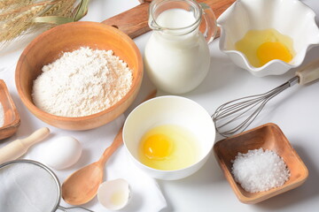 Frame of food ingredients for baking on a white background. Flour, eggs, sugar and milk in white and wooden bowls . Cooking and baking concept.
