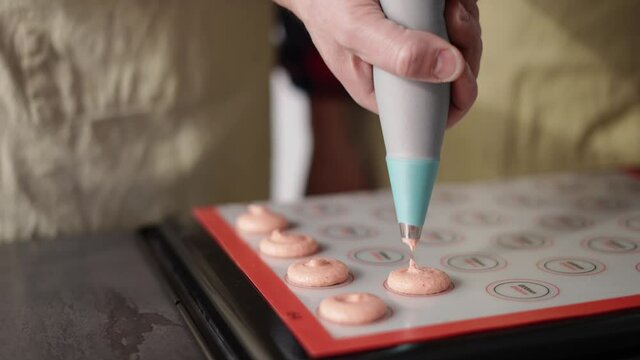 Piping out pink macaron mixture on a slip mat on backing tray, professional hands