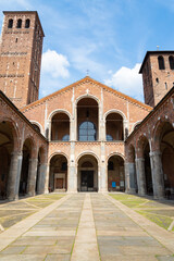 Fototapeta na wymiar Patio of the famous Sant'Ambrogio (meaning Saint Ambrogio) romanesque cathedral in Milan, Italy, with beautiful facade with arches and bell towers. Blue sky on the background.