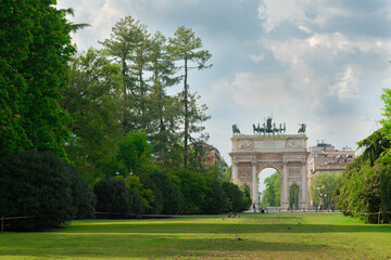 The famous "Arco della pace" (meaning "Arch of the peace) located in Milan, Italy, close to Sempione Park. Green grass in the foreground.
