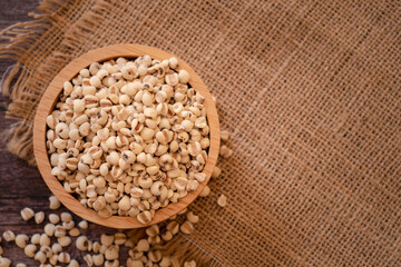 Bowl of Adlay millet or pearl millet or Job's tears in wooden bowl on the sackcloth over wooden table background. copy space for text. Healthy food.