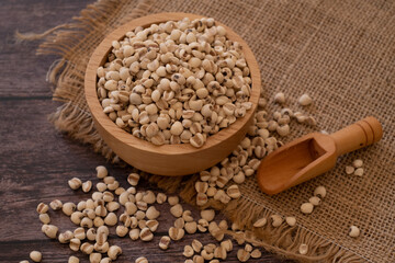 Bowl of Adlay millet or pearl millet or Job's tears in wooden bowl and wooden scoop on the sackcloth over wooden table background. copy space for text. Healthy food.
