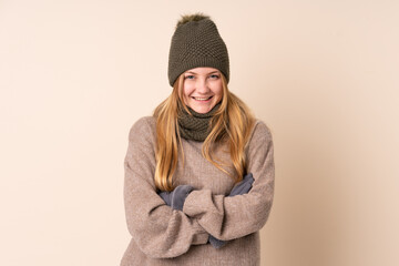 Teenager Ukrainian girl with winter hat isolated on beige background laughing