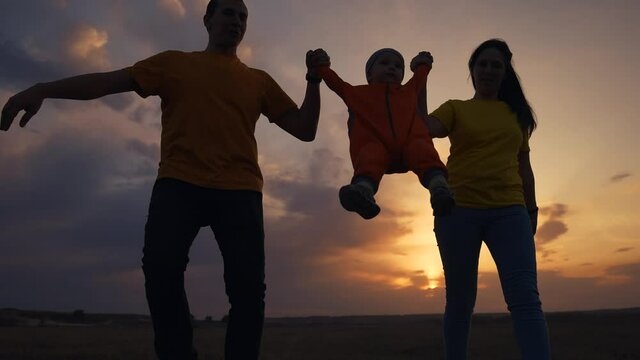happy family. father mother and baby run play at sunset silhouette holding hands and throw up fun. happy family in kid dream park concept. baby and parents family run together silhouette in the park