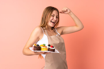 Pastry Ukrainian chef holding a muffins isolated on pink background celebrating a victory