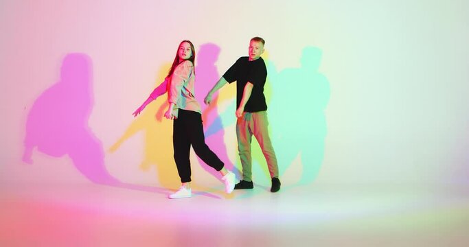 Cool dancing young couple synchronously moving in colourful studio light. Contemporary dance, hip hop dancers
