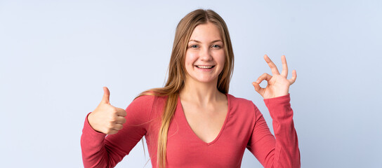 Naklejka na ściany i meble Teenager Ukrainian girl isolated on blue background showing ok sign and thumb up gesture
