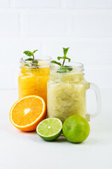 Orange and lime smoothie with mint in glass cups and halved fruit