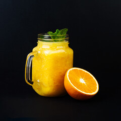 Orange smoothie with mint in glass cup and halved fruit