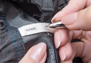 Pen in mother's hands for fills the Name label on children's school clothes. Child name, concept
