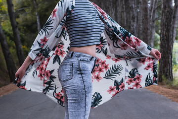 Woman dancing in a beautiful road surrounded by trees with a flowers shirt 