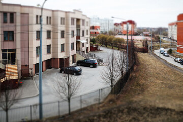City street with houses and cars, cloudy weather, tilt shift effect.