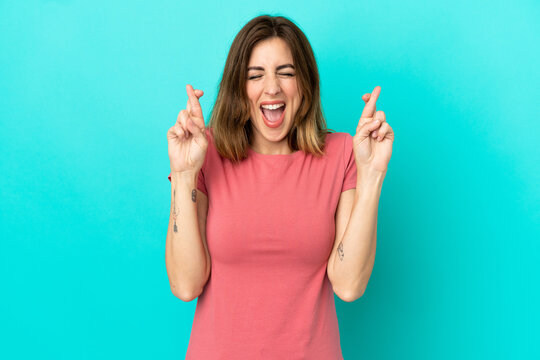 Young caucasian woman isolated on blue background with fingers crossing