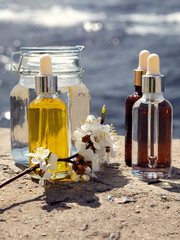 Bottles with cosmetic serum, a container with infusion and a sprig of blossoming apricot on a natural background. Sunlight, selective focus, natural cosmetics. Body and face care. 