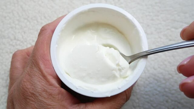 A glass with curd mass in female hands.  Female hands with a spoon take out the curd mass from the glass.  Snack, dessert, baby food