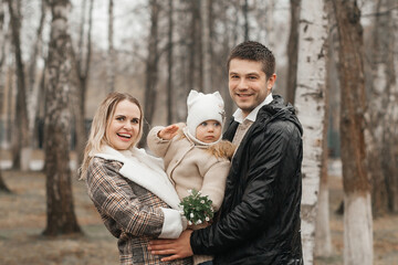 A young, beautiful couple is walking in the park with their little daughter.
