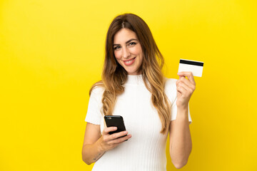 Naklejka premium Caucasian woman isolated on yellow background buying with the mobile with a credit card