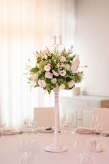 Centerpiece made of green leaves and fresh flowers stands on the dinner table. Wedding day. Fresh flowers decorations.