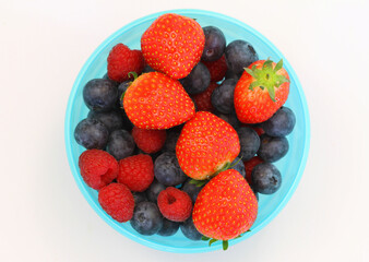 Selection of fresh forest fruits and strawberries in blue plastic bowl on white background, best source of Vitamin C

