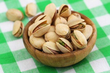Pistachio nuts in wooden bowl on checkered cloth, closeup
