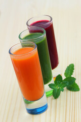 Carrot, spinach and beetroot smooties in transparent tall glasses on wooden surface
