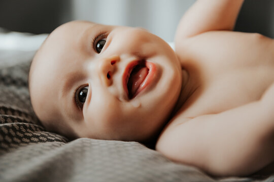 Beautiful cute baby lying and playing on the bed in the room, photo with daylight from the window