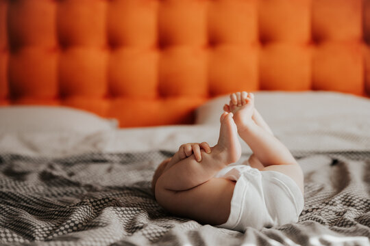 Beautiful cute baby lying and playing on the bed in the room, photo with daylight from the window