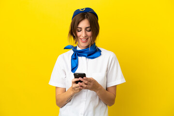 Airplane stewardess woman isolated on yellow background sending a message with the mobile