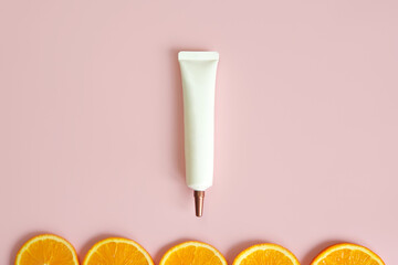 Top view of face and eye cream squeeze, natural cosmetic tube with long nozzle and bronze screw cap and orange slices on pink background. Mockup, template. Skincare and beauty concept