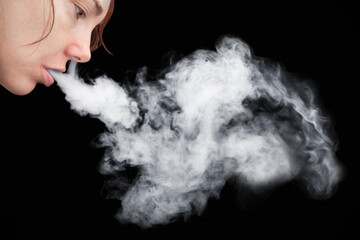 Face profile of young woman smoking with thick white smoke from mouth on black background.