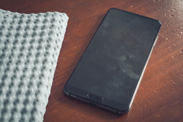 Cleaning Wipe And A Smartphone Screen With Dust, Dirt And Fingerprints On A Table