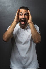 Man wearing a white tshirt over a grey background with his hand next to his head and looking surprised