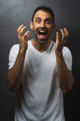 Man wearing a white tshirt over a grey background looking surprised