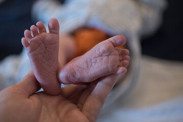 Hand hält Füße eines Neugeborenen oder gibt Babymassage, Baby liegt auf Boden und trägt orange Stoffwindel und weißes Obertreil - obrazy, fototapety, plakaty