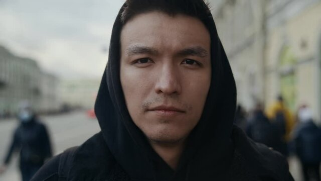 Portrait Attractive young Asian male. A guy in a black hoodie stands in the middle of a busy street looking at the camera. Black hood on the head