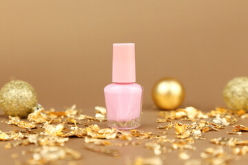 Nail polish small glass bottle, gold paper pieces and Christmas balls on golden background. Unbranded mockup with copy space. Professional manicure concept.