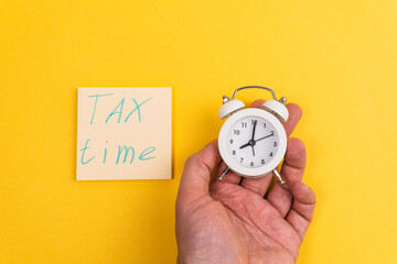 Tax time written with an alarm clock on yellow background. Tax payment reminder or annual taxation concept.