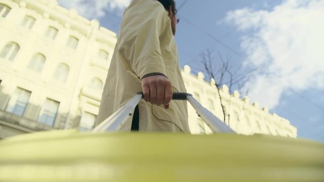 camera rigged on a yellow travel suitcase with a long handle. A man in a yellow raincoat or trench coat looks around and continues to move around the city street. Sunny day and blue sky