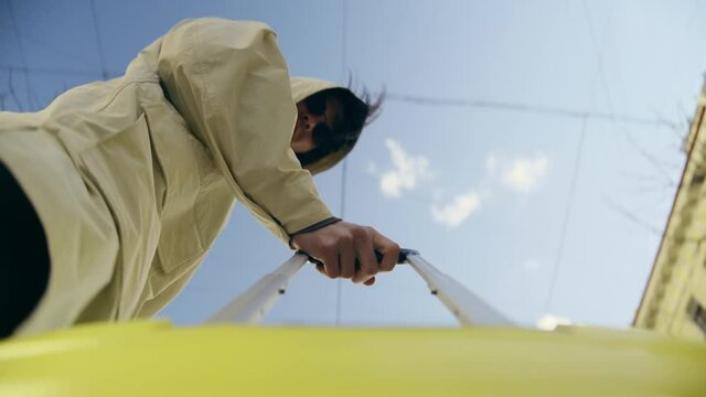 camera rigged on yellow travel suitcase with a long handle. A man in a yellow raincoat or trench coat looks at camera and continues to move around the city street. Sunny day and blue sky. Clear frame